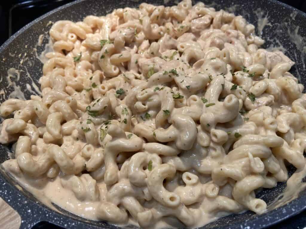 Sauteed chicken with alfredo sauce and shredded cheese and pasta in a pan