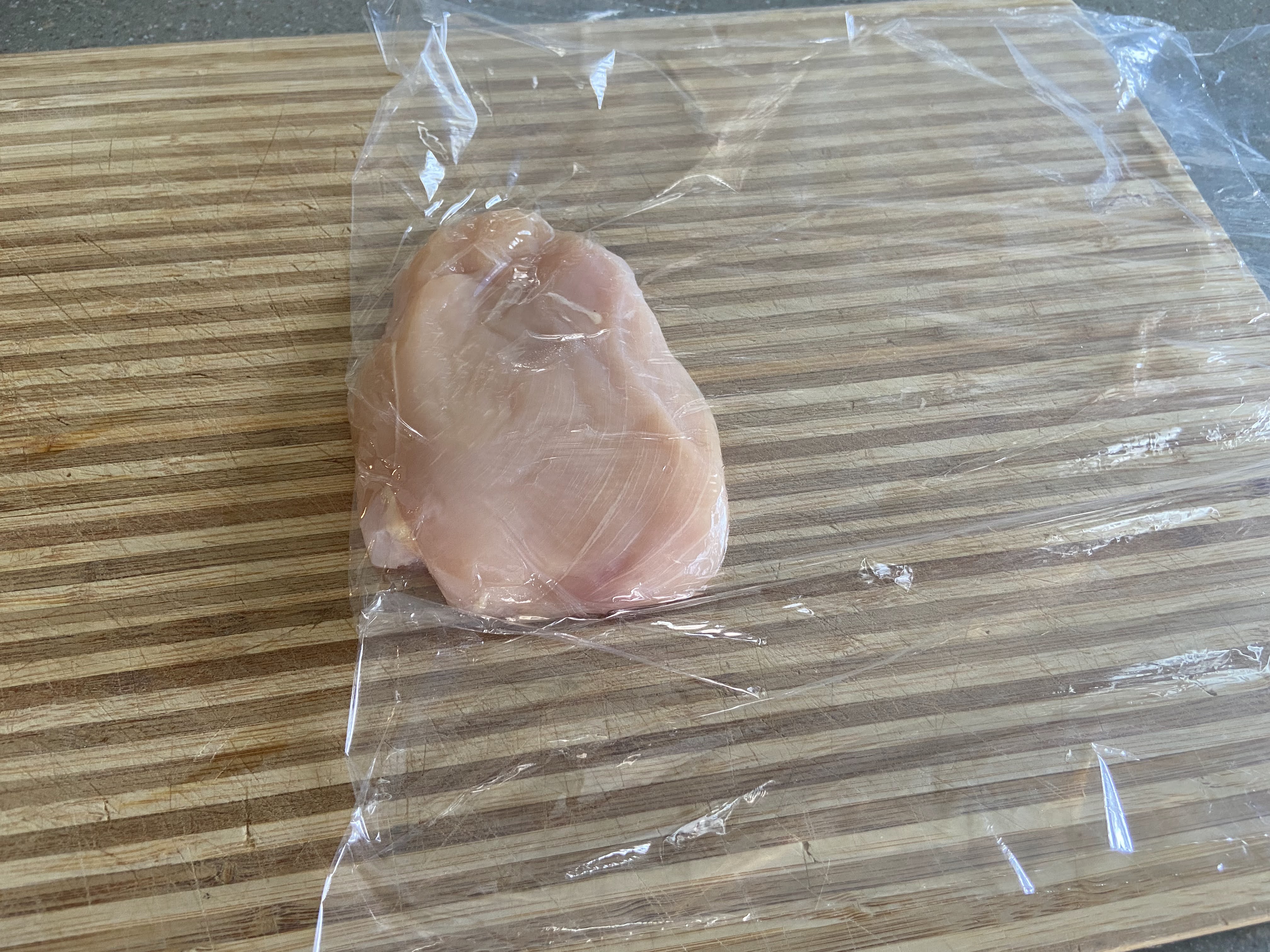 chicken cutlet placed on a cutting board wrapped in clear foil