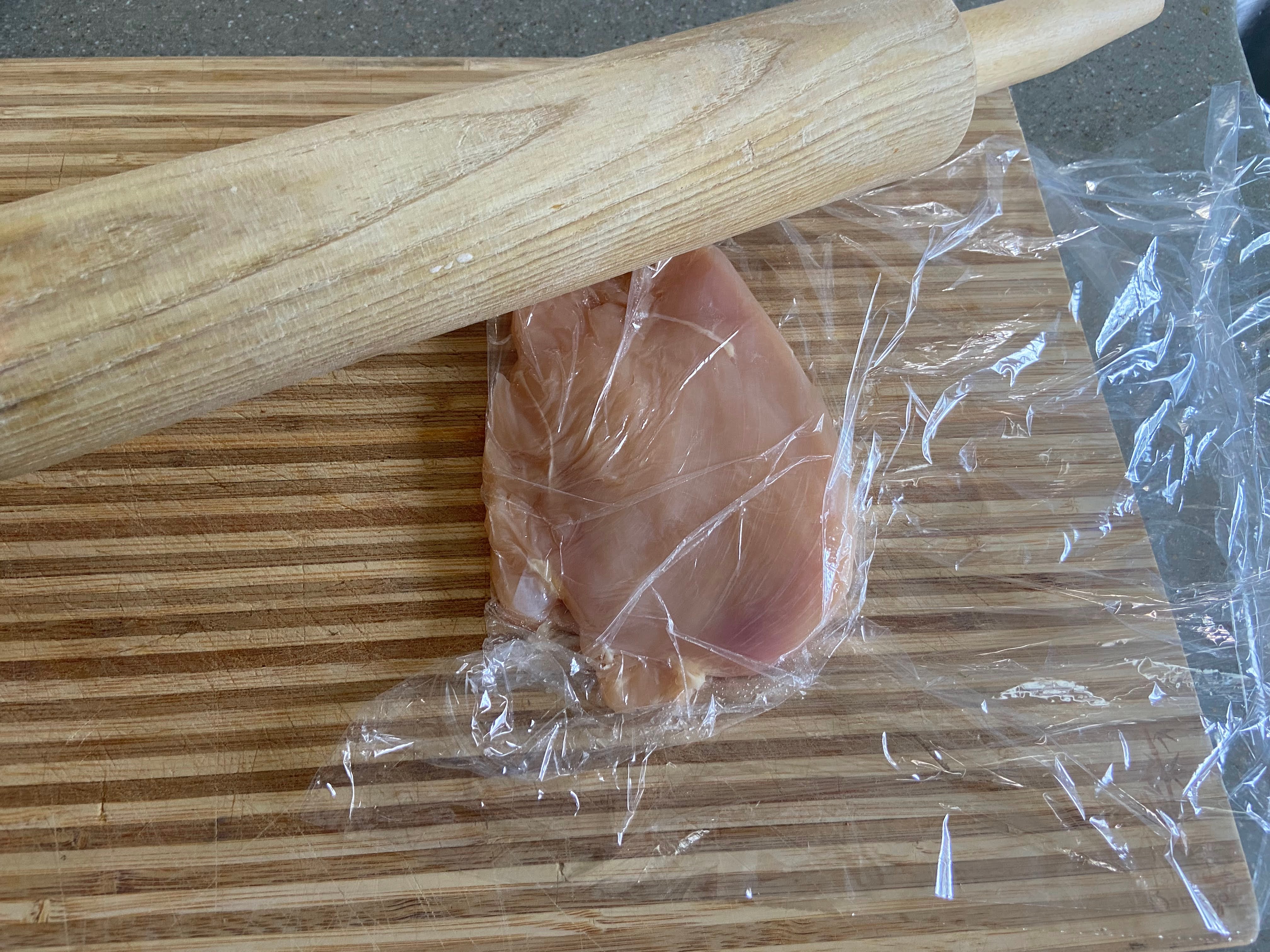 chicken cutlet placed on a cutting board wrapped in clear foil pounded with a rolling pin. 