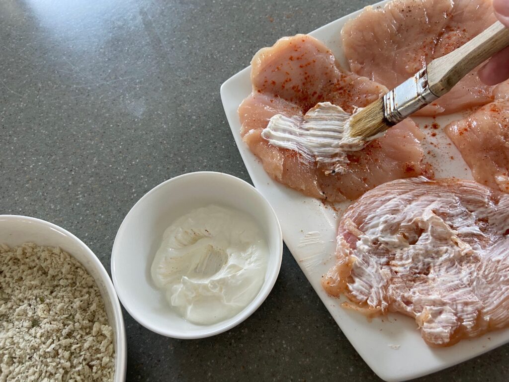 chicken cutlets are coater with sour cream using a brush. 