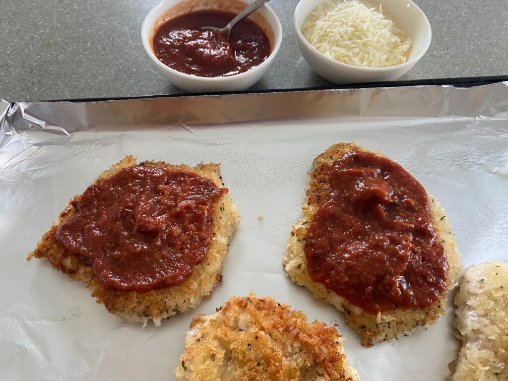 Chicken cutlets added to a foiled lined baking sheet and covered with tomato sauce 