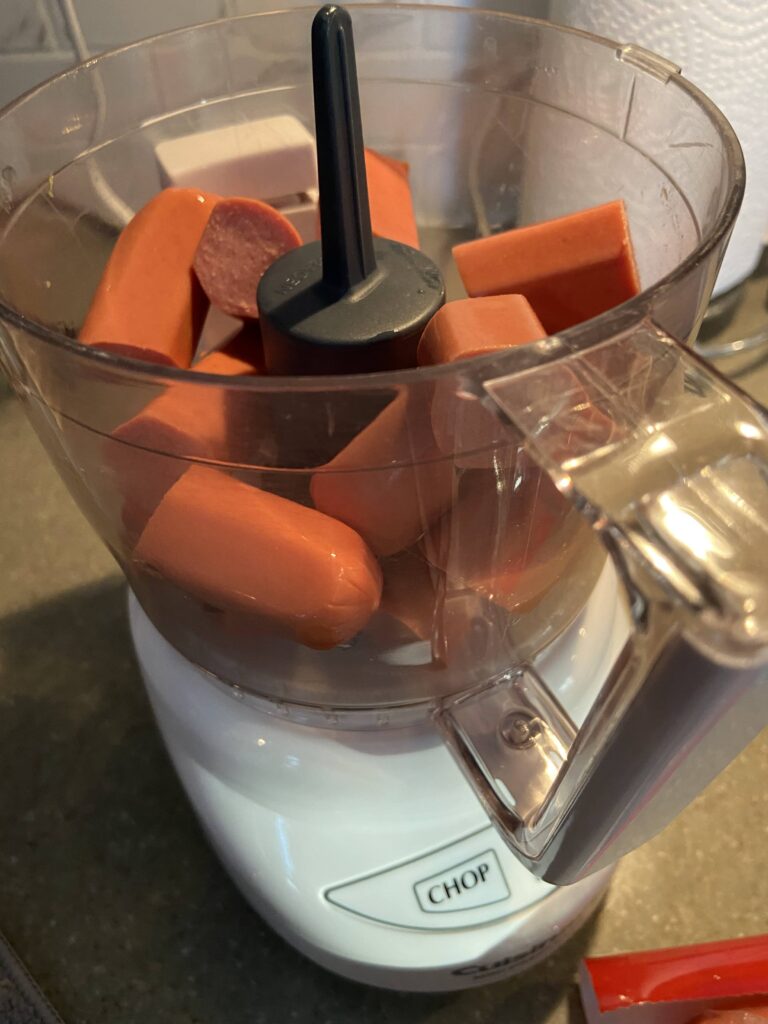 hot dogs cut up in pieces are added to the small food chopper