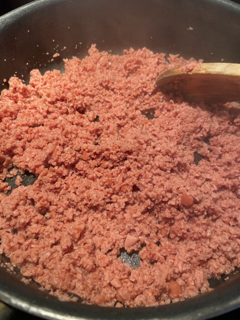 Finely chopped hot dogs are added to a pan with a drizzle of oil
Sauteed hot dogs