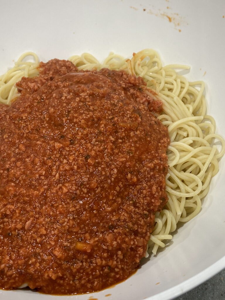 Cooked spaghetti are added to a serving dish
Tomato meat sauce is added to the spaghetti