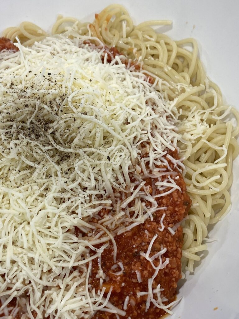 Cooked spaghetti are added to a serving dish
Tomato meat sauce is added to the spaghetti and then shredded cheese is added is aded on top.
