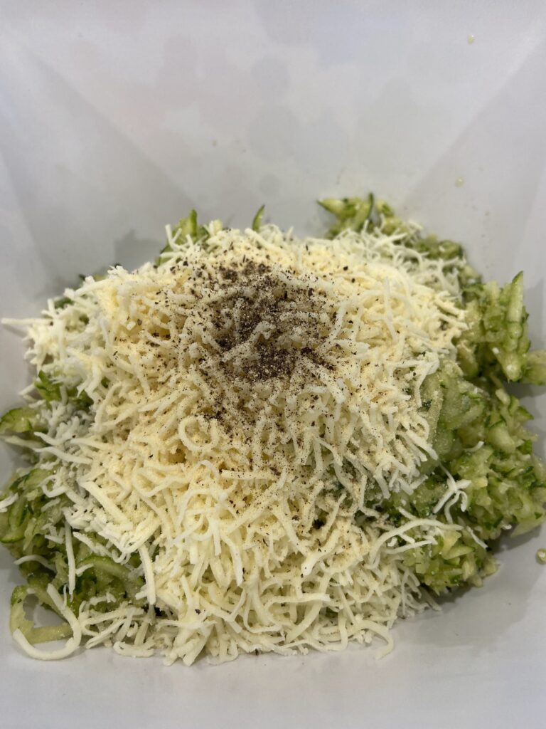 shredded zucchini in a bowl and a cracked egg on top and added shredded cheese