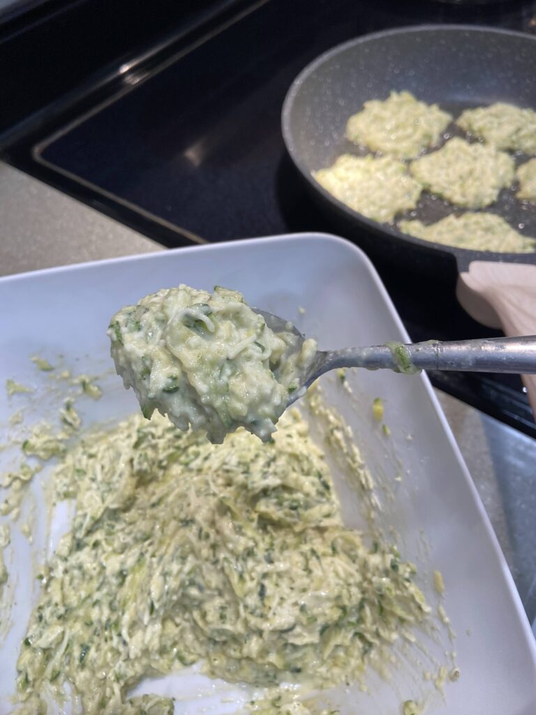 Using a spoonful the zucchini mixture is added to the cooking pan  