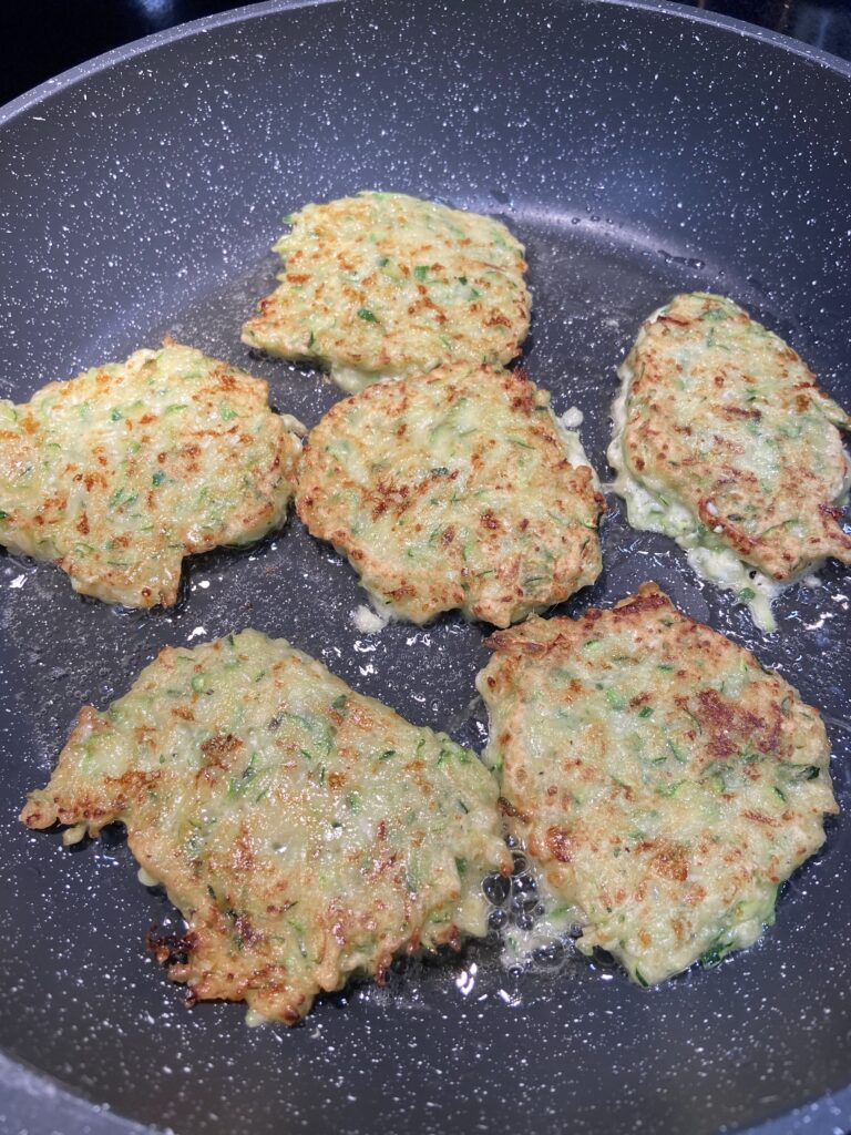Zucchini fritters are cooking in a pan