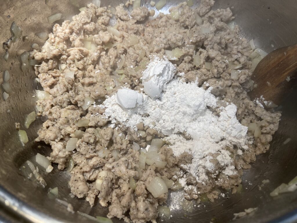 Ground chicken sausage sautéed in pot with chopped onions and flour