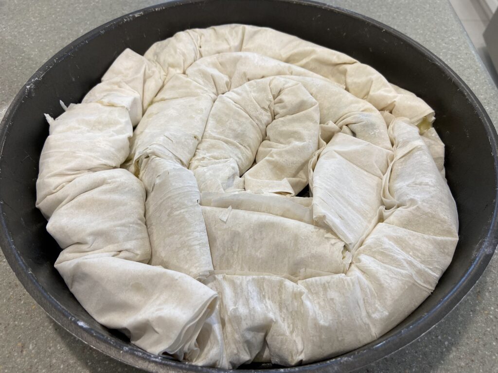 Filled phyllo (filo) pastry sheets are arranged in a circle in the round baking pan