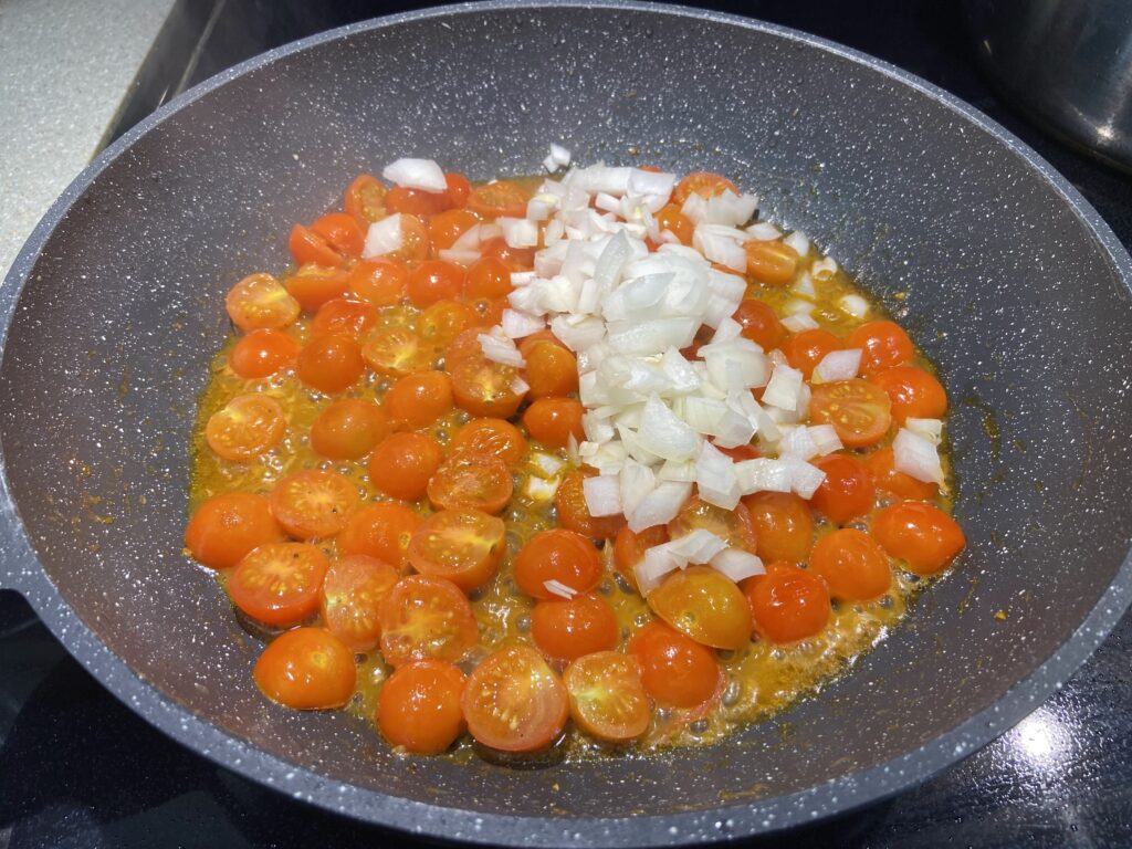 blistered cherry tomatoes in a pan with olive oil and cooped onion