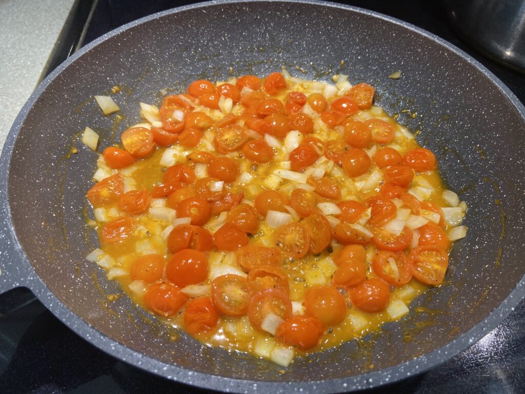 blistered cherry tomatoes in a pan with olive oil and cooped onion