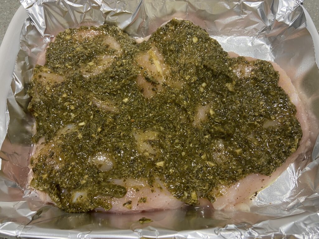 pesto spread out on top of seasoned chicken breast cutlets arranged in a baking dish