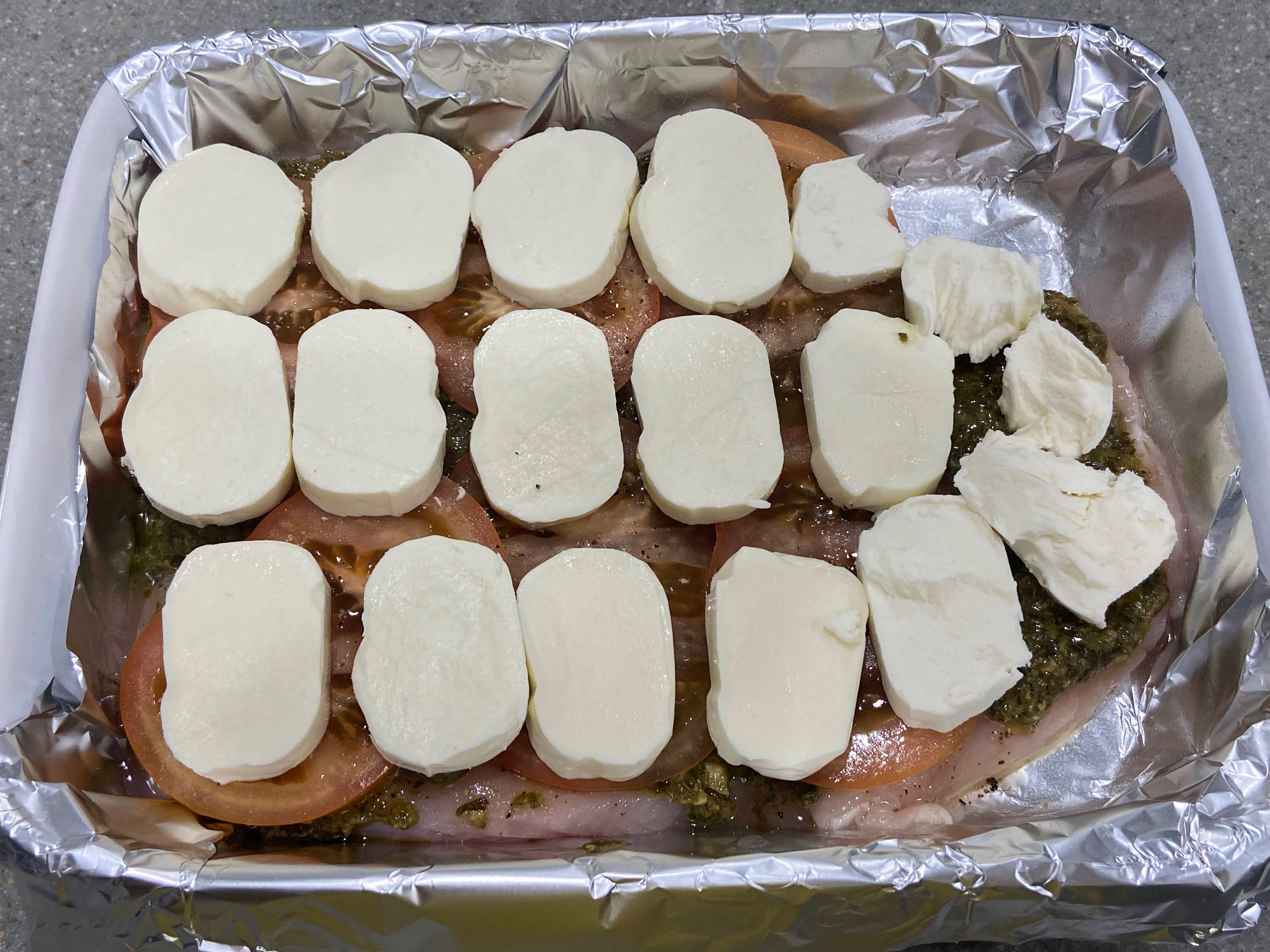 fresh mozzarella cheese slices arranged on top of pesto spread out on top of seasoned chicken breast cutlets arranged in a baking dish