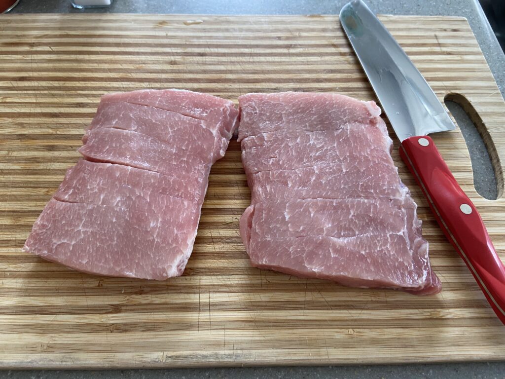 pork shoulder cut into cubes on a cutting board with a knife