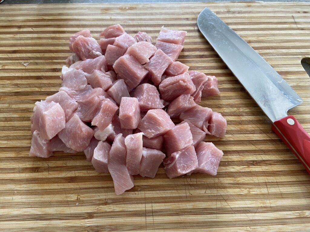 pork shoulder cut into cubes on a cutting board with a knife